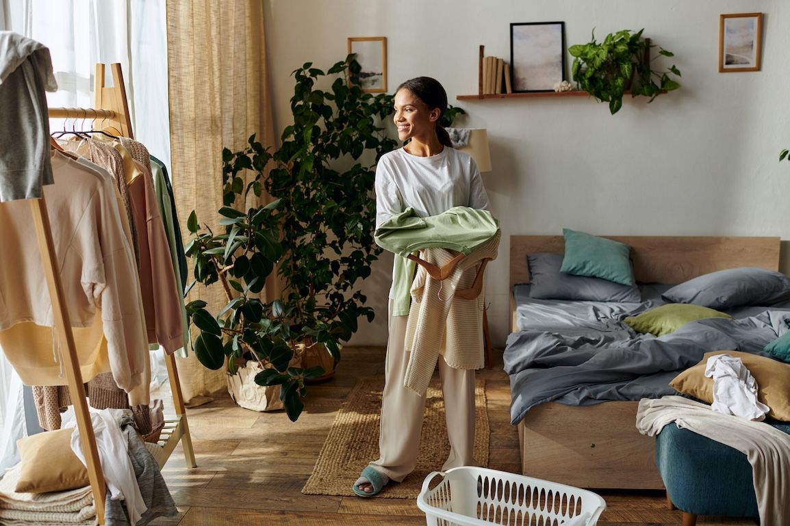 Woman organizing laundry in a cozy bedroom, holding folded clothes and surrounded by winter wear