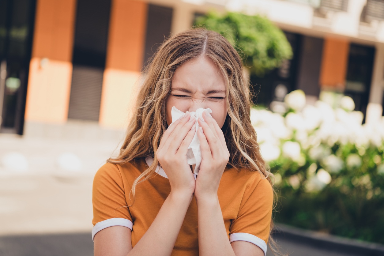 Woman sneezing outdoors due to spring allergies and pollen exposure