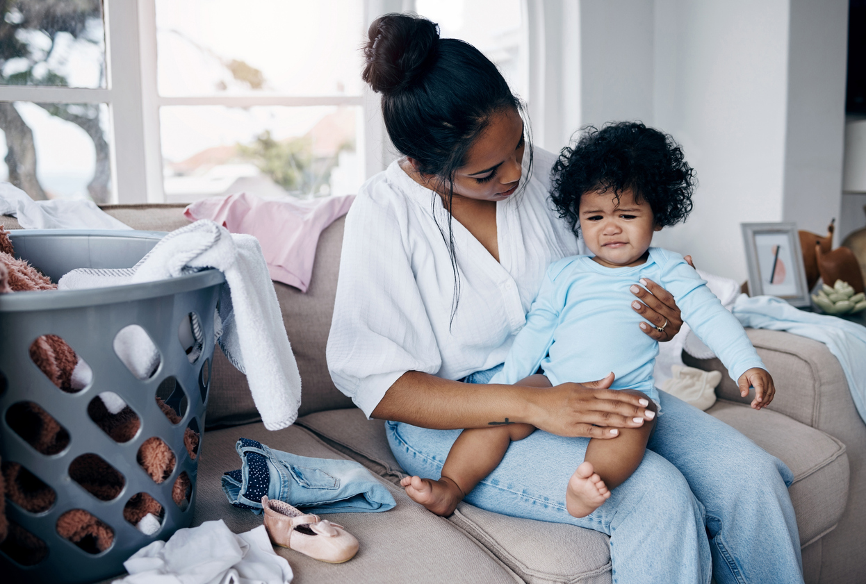 Busy mother sitting next to laundry basket while managing household responsibilities